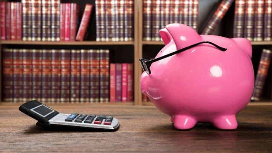 A pink piggy bank with glasses looking at a calculator. 