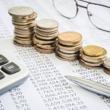 Pair of glasses that faces stacks of coins, a pen, and a calculator, on top of a sheet of paper with calculations. 