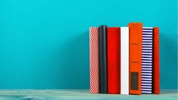 Seven proofreading reference books standing upright against a teal background.