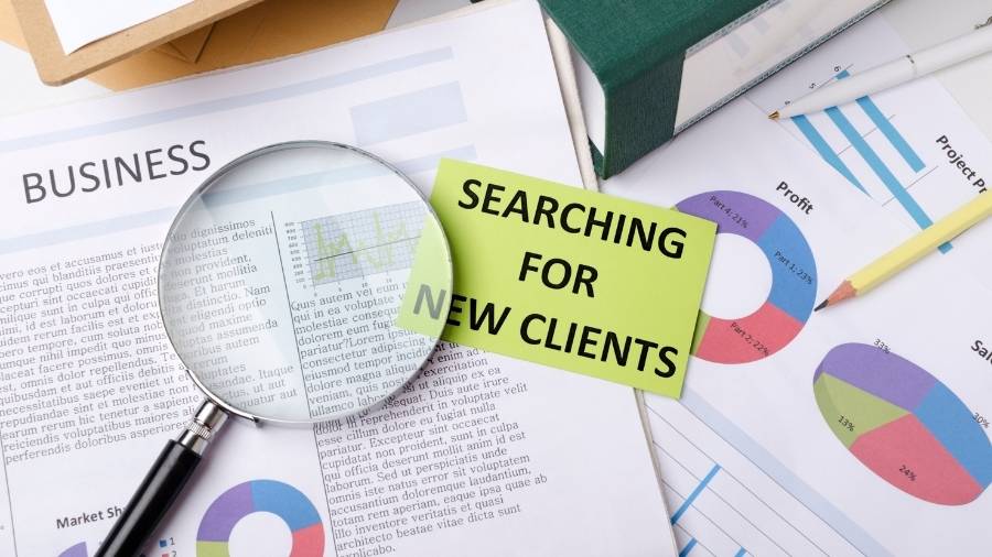 A magnifying glass and a small paper with the words "Searching For New Clients." 