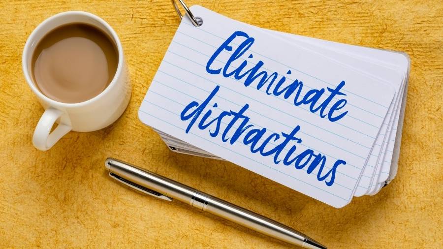 A writing pen, a mug of coffee, and a notecard with the message "Eliminate distractions." 