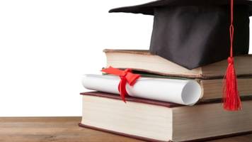 A graduate hat, a certificate, and three books sitting on a wooden desk. 