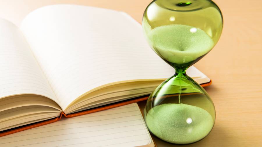 A green-tinged hourglass sand timer and two notebooks atop a wooden desk.