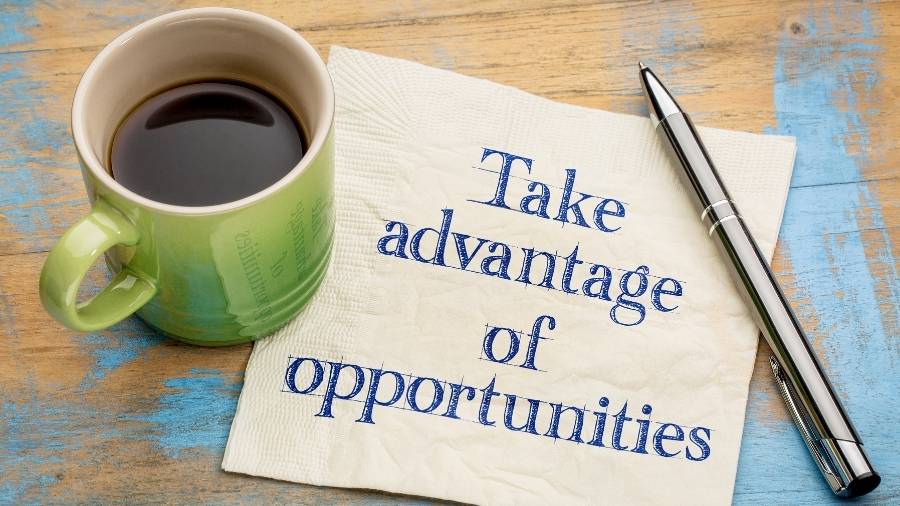 A coffee mug, a writing pen, and a napkin with the message "Take advantage of opportunities" sit on a wooden table. 