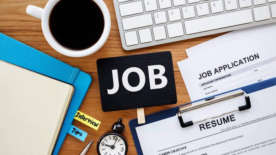 A job application and résumé are sitting on a wooden desk. There's also a folder with tabs that say "interview" and "tips." 