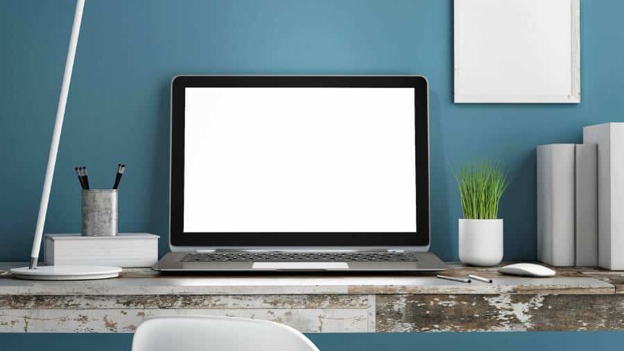 A laptop, various books, a container with pencils, and a little green plant sit on an industrial-looking desk. 