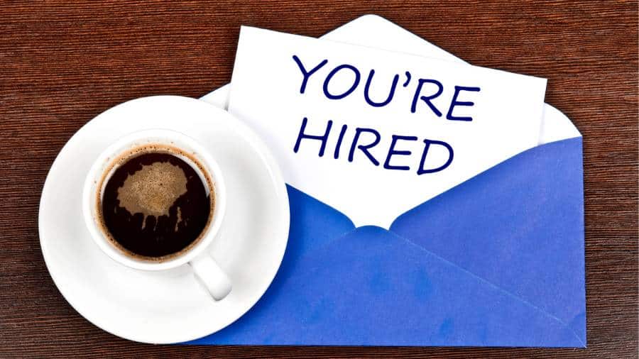 A coffee mug and an open envelope with a message inside that says "You're Hired." 