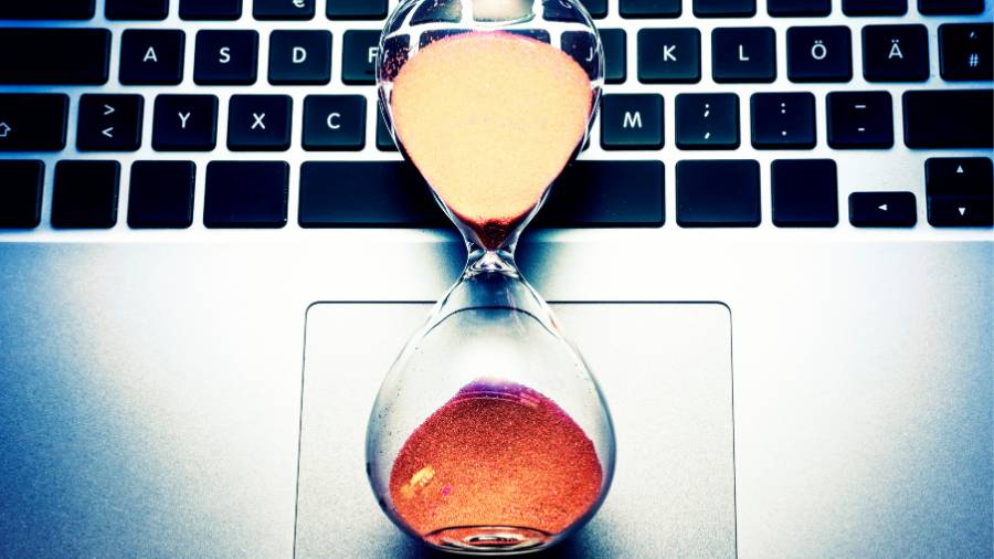 A sand timer lying on a laptop keyboard. 